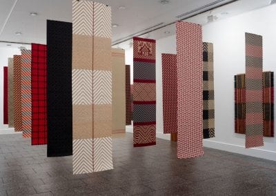 Gallery interior with multiple hanging vertical textile works in red and earth tones