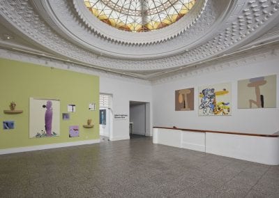 Installation view of gallery interior with Art Deco dome glass ceiling and paintings on walls