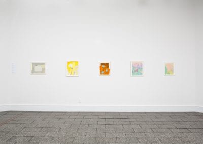 A row of five small pastel abstract paintings on a white wall