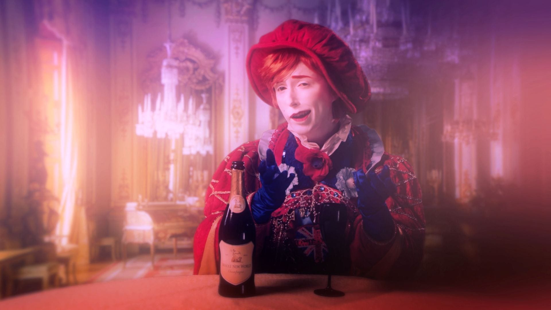 A young man sits at a table, dressed in garish expensive clothes including a red tam o' shanter hat and cape. He talks smugly to the camera. Next to him is a bottle of alcohol.