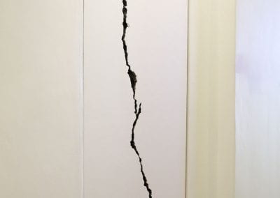 A tall white wall with a huge, long dark crack opening up across the length of the wall.