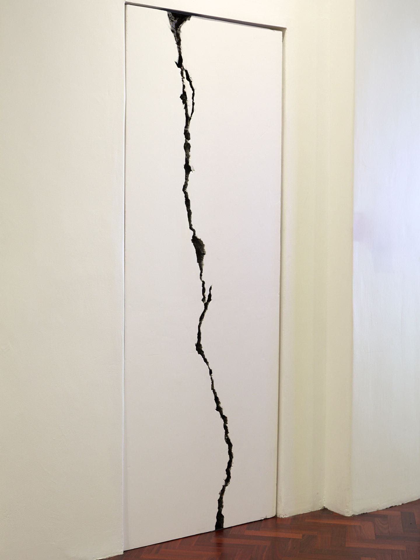 A tall white wall with a huge, long dark crack opening up across the length of the wall.