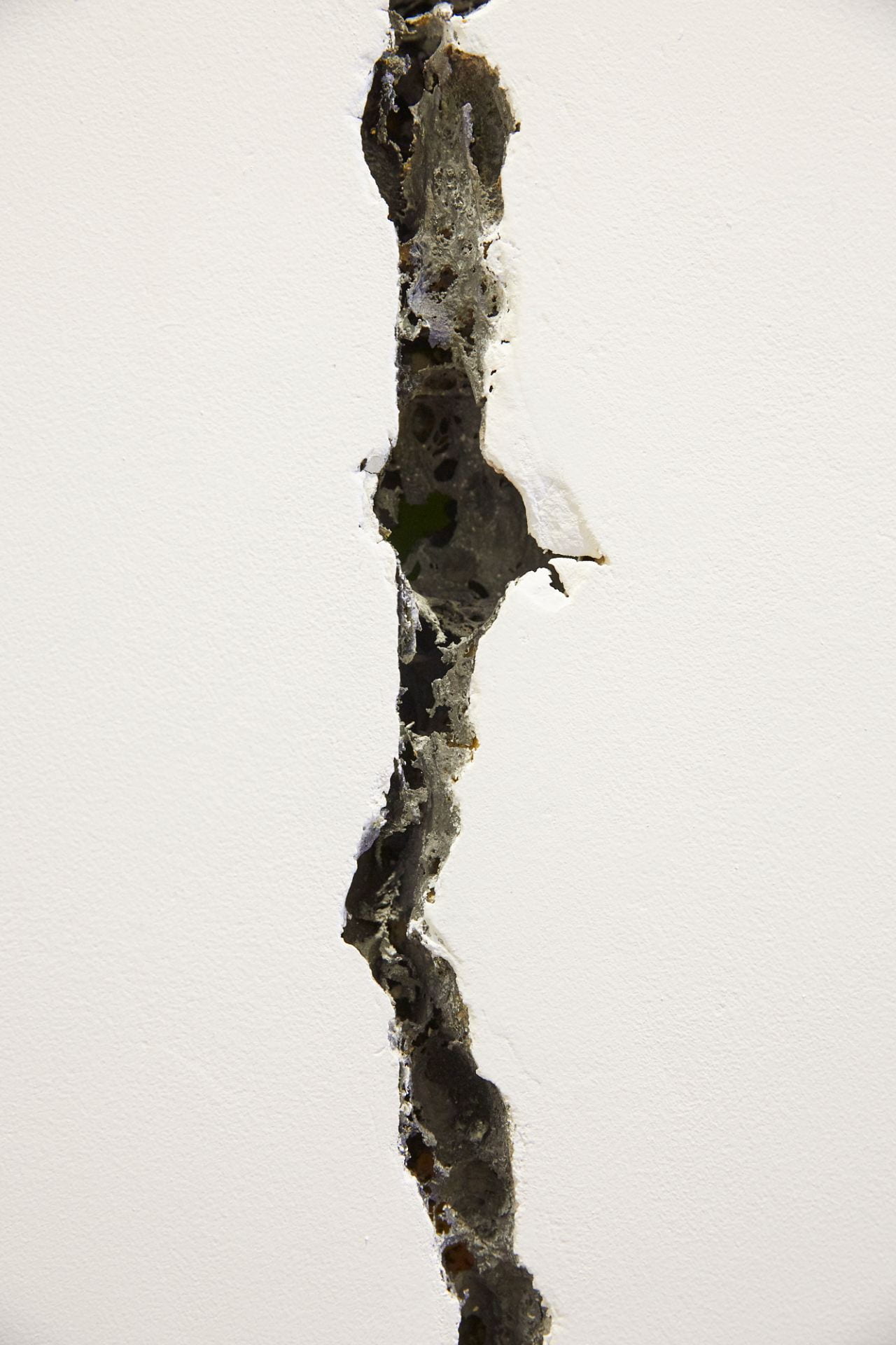 Close-up of a wide, deep, dark crack in a white wall.