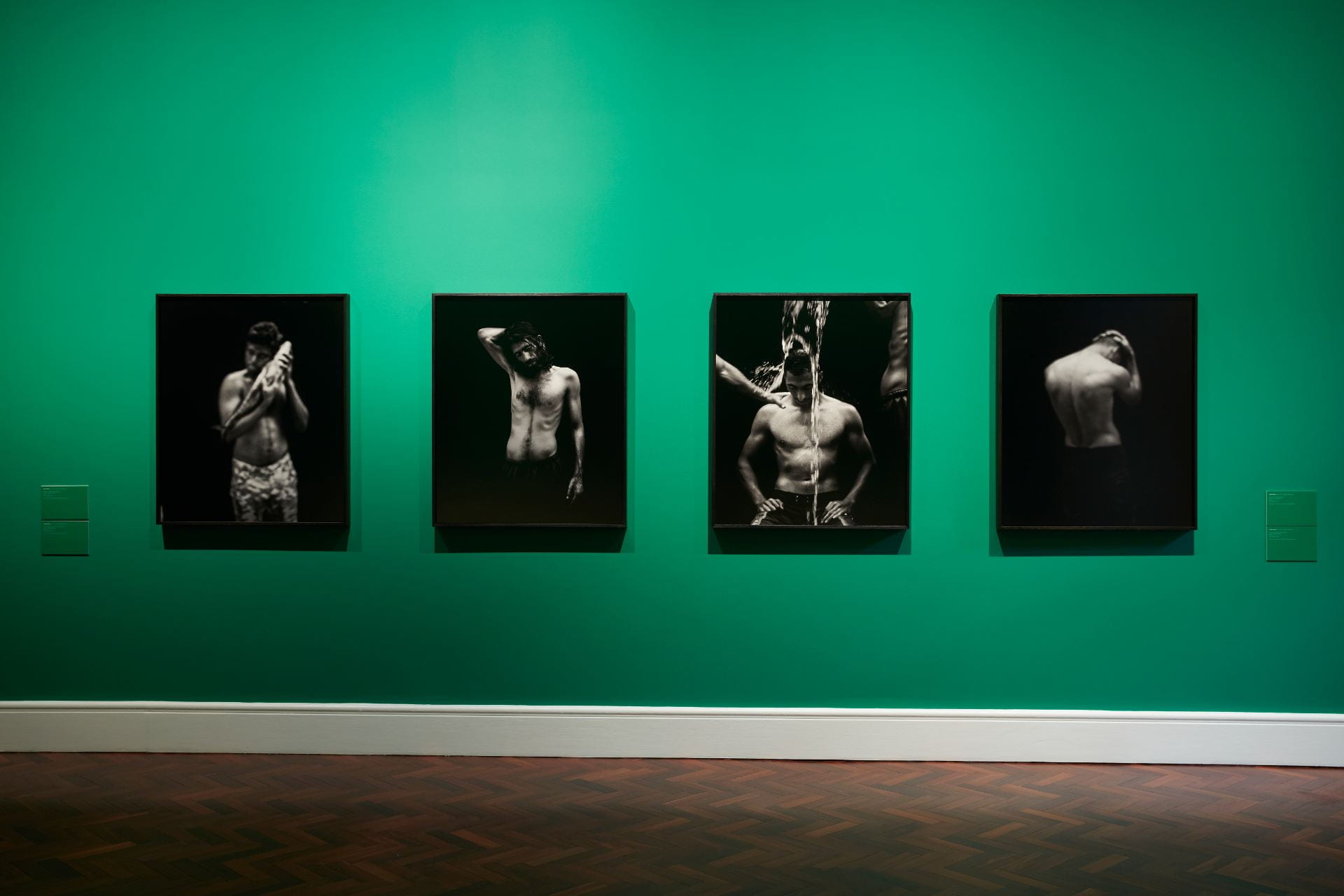 A deep green wall with four black and white portraits of Manus Island refugees hung on it.