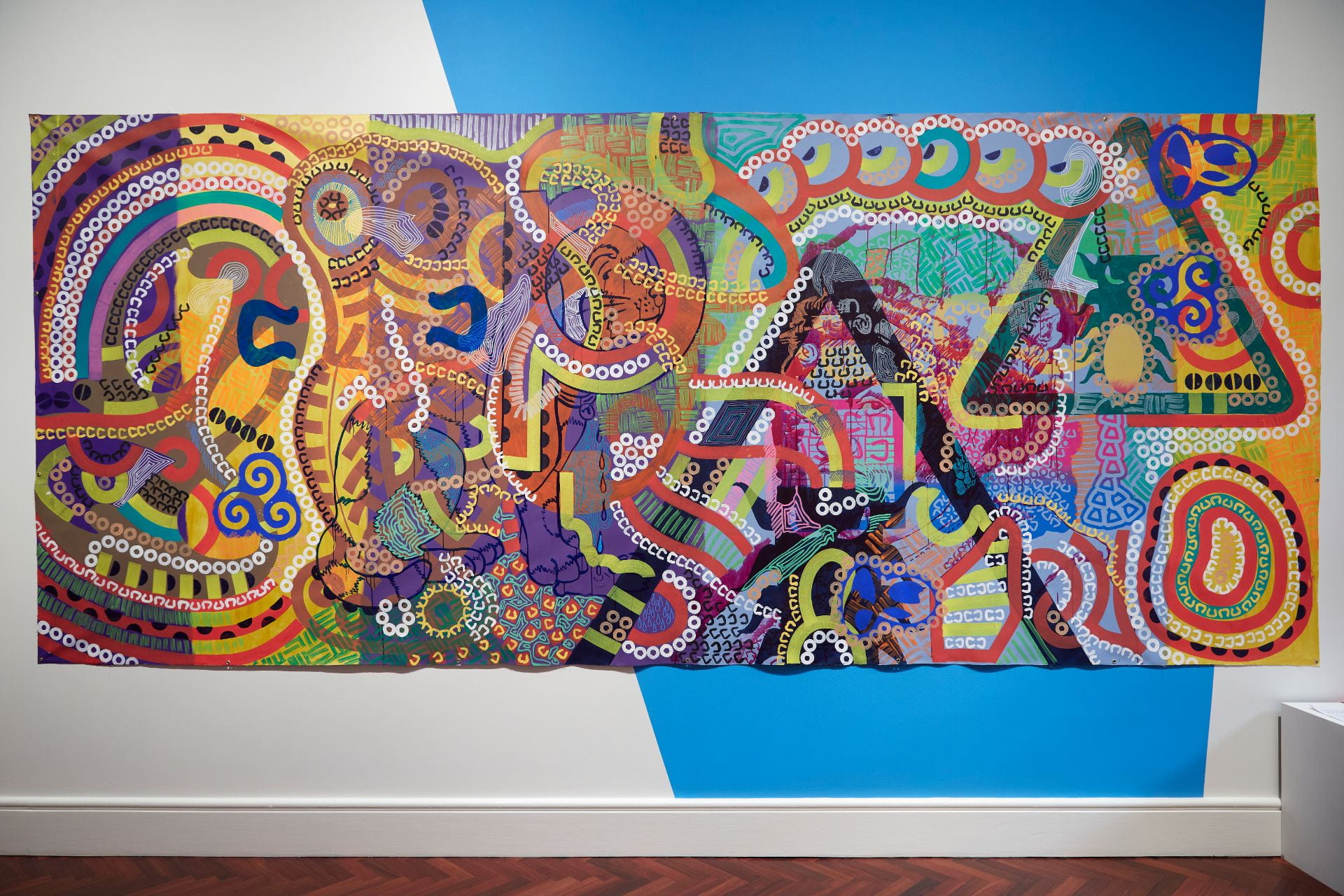A large rectangular painting hanging on a wall. The painting is filled with curved patterns, shapes and colors.