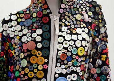 A close-up of a mannequin wearing a onesie covered in buttons of all different shapes, colours and sizes.