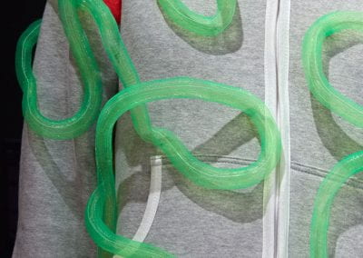 Close-up of a grey onesie with abstract red shapes and green tubing sewn onto it.