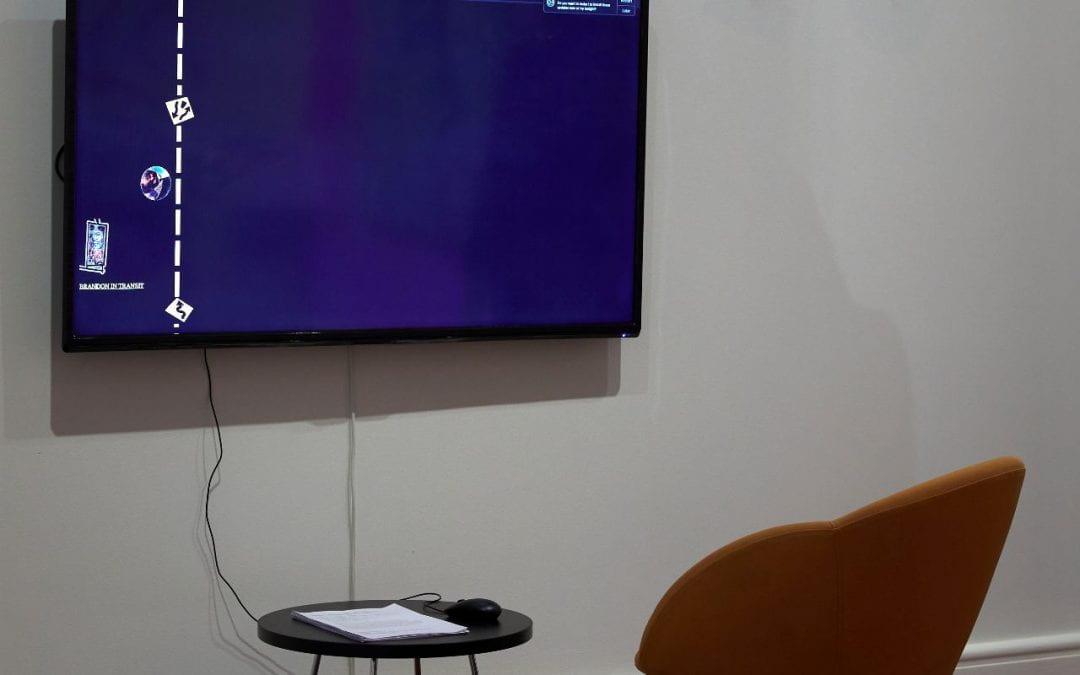 A TV with an orange chair and black table next to it. The TV shows a black website with a roadmap on it.