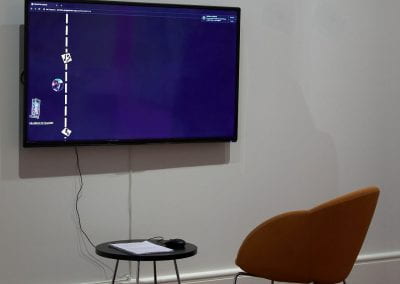 A TV with an orange chair and black table next to it. The TV shows a black website with a roadmap on it.