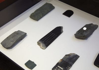 Close-up of greenstone sculptures carved to look like television remotes, with pieces chipped off and rough ends exposed.