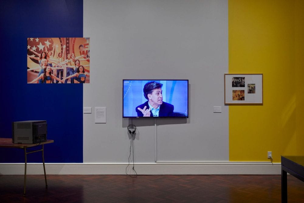 A flatscreen television showing a man in a suit looking to the right. The walls behind the TV are blue, white and yellow.