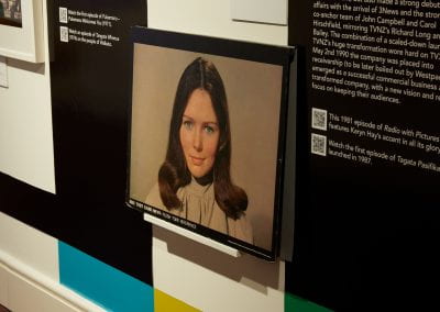 A stiff card picture sitting on a front-facing shelf in a display. Depicted is a woman with dark hair looking directly at the camera. A light grey background is behind her.