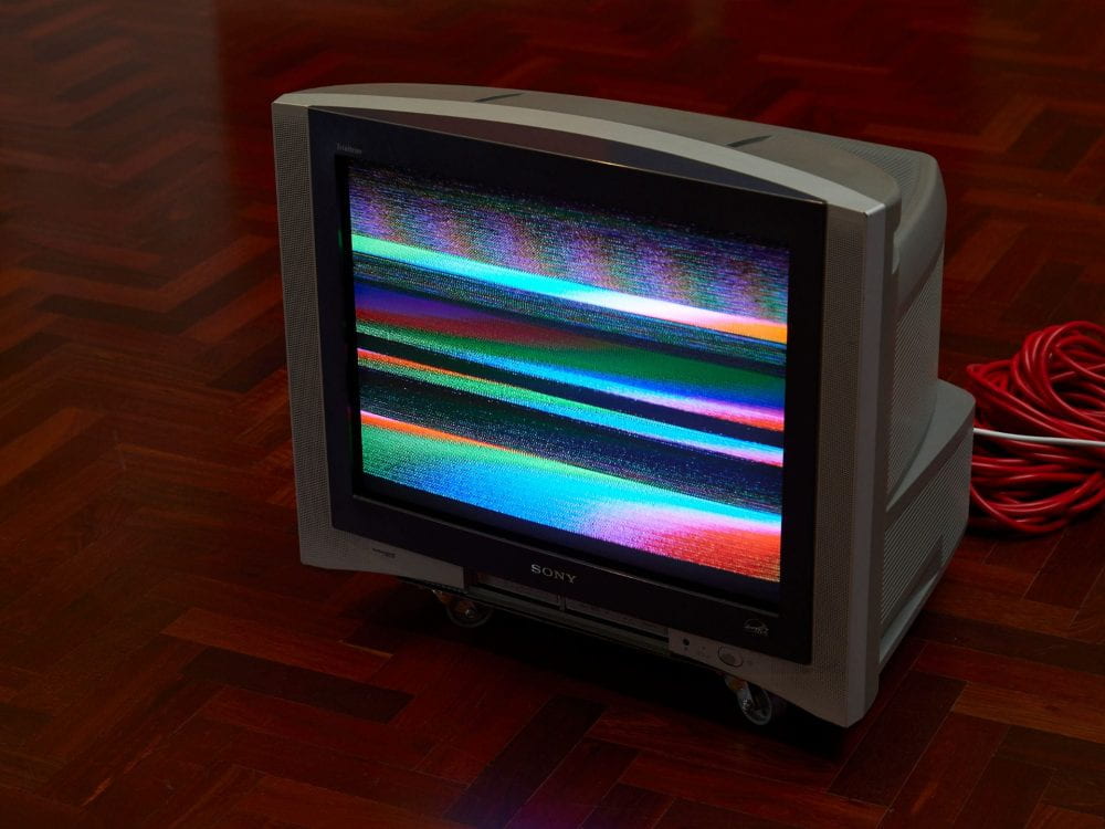 A CRT television set with jumbled multi-colored bands running across the screen, as a result of TV aerial interference.