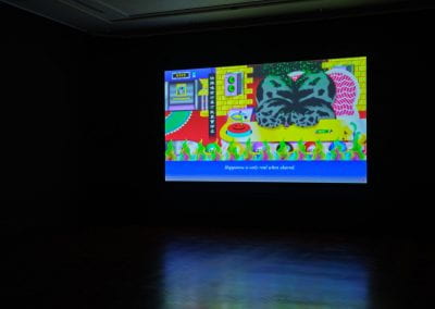 A film projected in a dark room. The film shows a bright animation of a cartoon cow surrounded by green flames, slow cooked into high-quality beef. The subtitle along the bottom of the film reads "happiness is only real when shared".