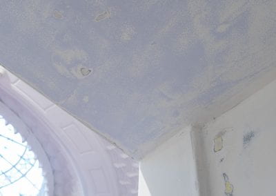 Close-up of the interior Booth walls, which have been sanded down to reveal layers of yellow paint in patches underneath. A stained glass heritage dome is visible in the background.