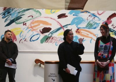 Three people stand talking in front of a colourful, abstract painting