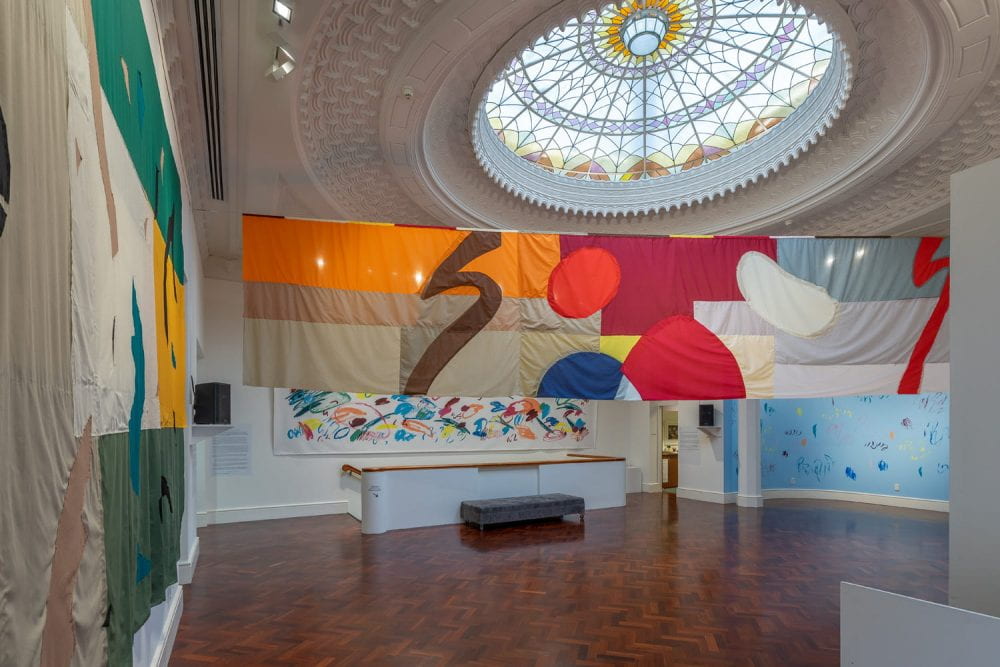 Large textile collage banner suspended in heritage building foyer with ornate dome glass ceiling