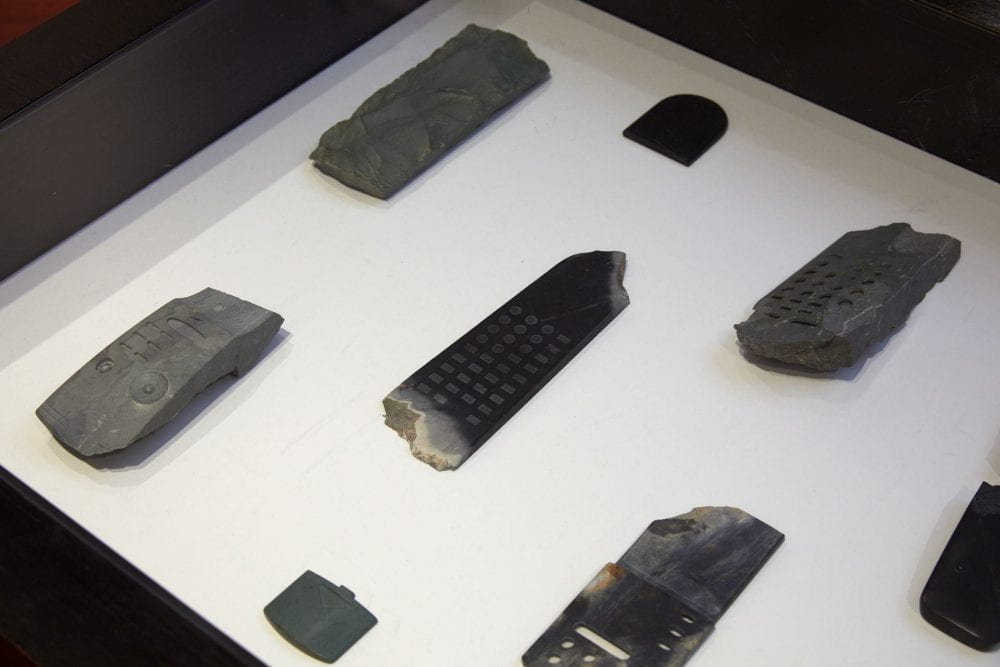 A glass case displaying pieces of greenstone carved to look like television remote controls.