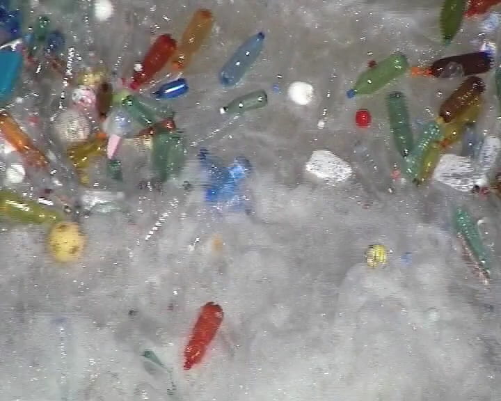 Lots of colourful plastic bottles surge and churn around in frothing white water.