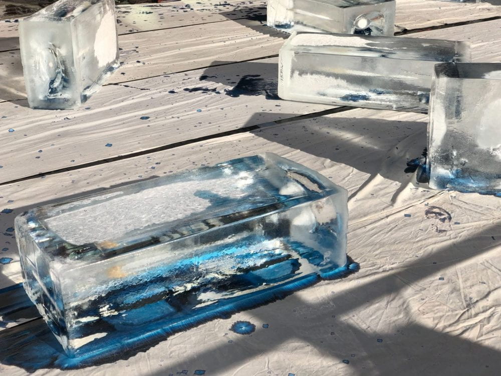 Several huge blocks of ice sit on spread out sheets of cloth. The ice is slowly melting onto the cloth, turning it blue where the water soaks in.