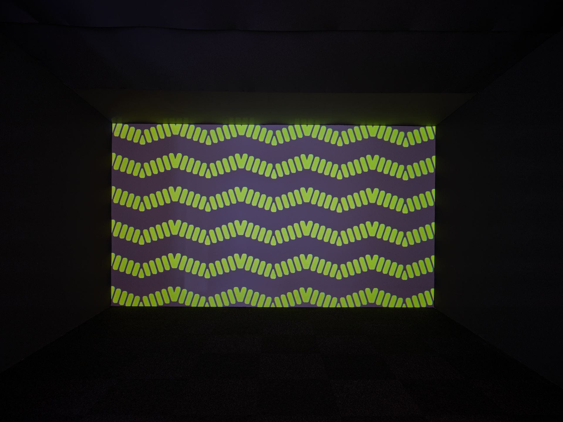 A film work filled with bright green patterns is contained within a dark film booth in the gallery space.