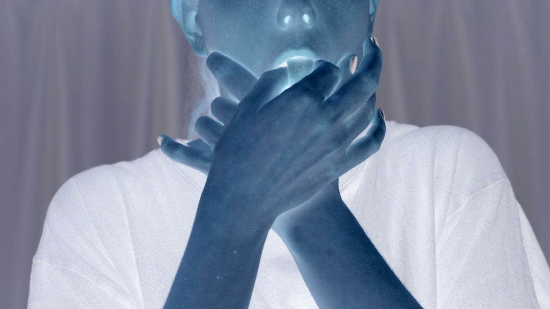 An inverted colour image of a person putting their hands into their mouth, grabbing their tongue.