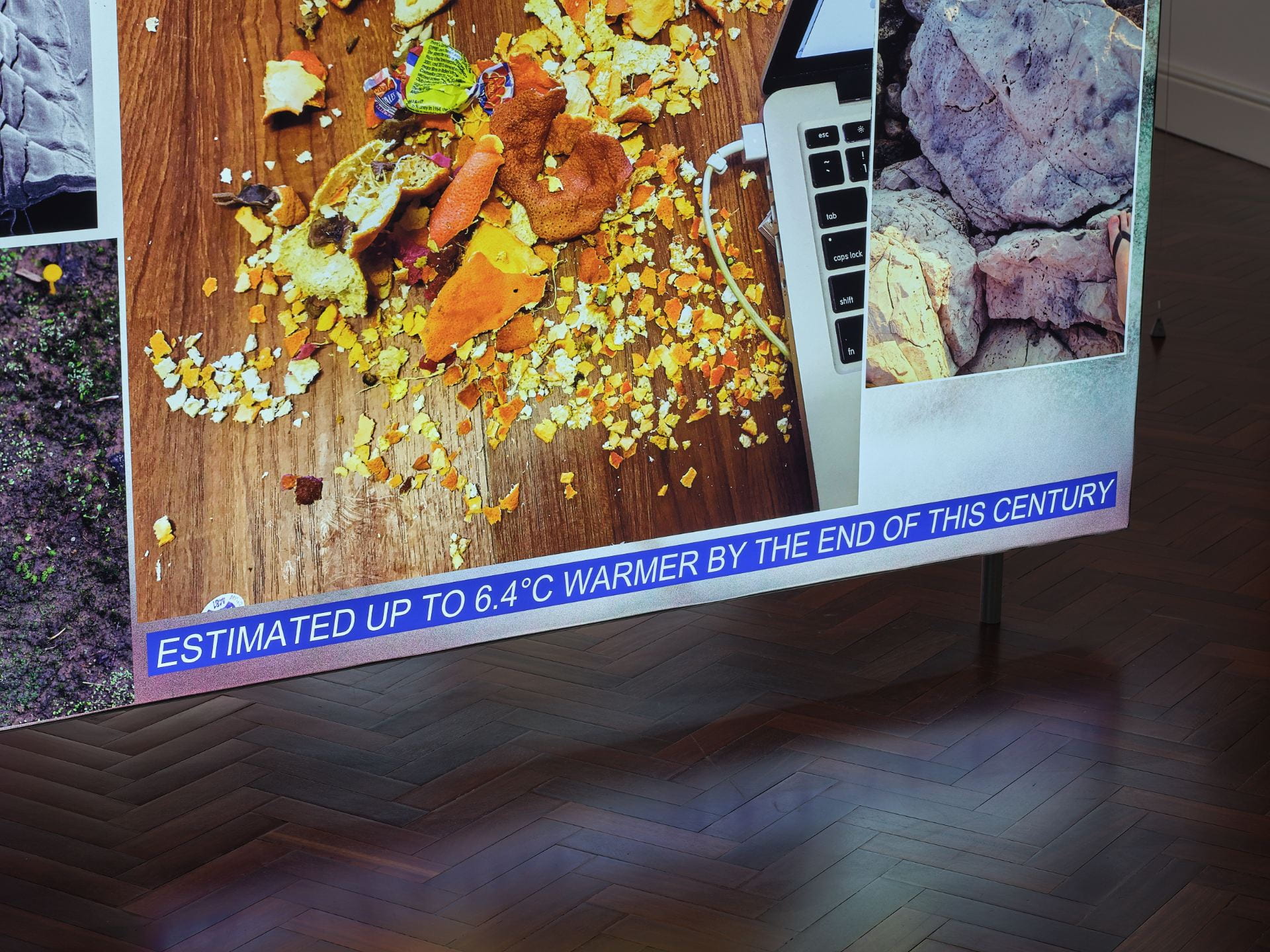 Close up of a lightbox. The lightbox has a series of jumbled pictures on it. The visible one is of a laptop with shredded mandarin peels and rubbish next to it, while some text below reads 'Estimated up to 6.4 degrees Celsius warmer by the end of this century'.