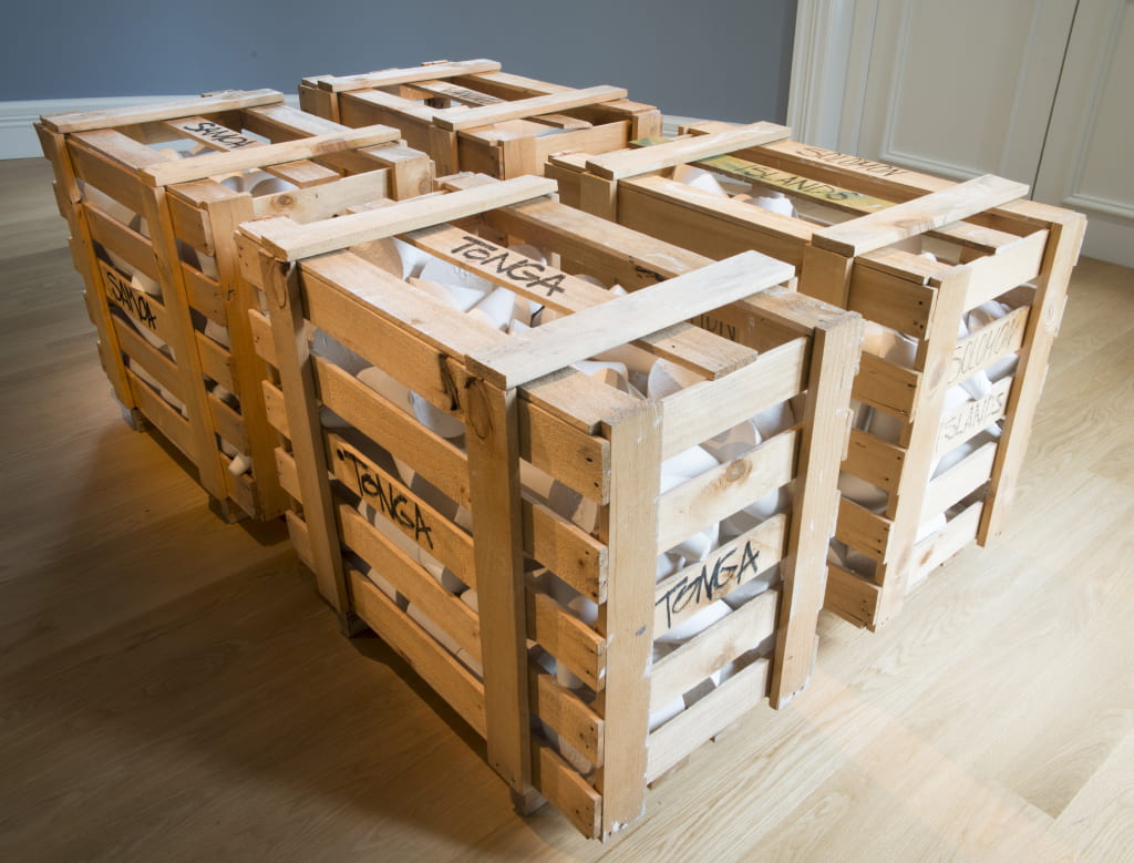 Four wooden pallets are arranged in a square formation, each containing plaster-cast taros. Each pallet has the name of a different Pacific country written on every side.