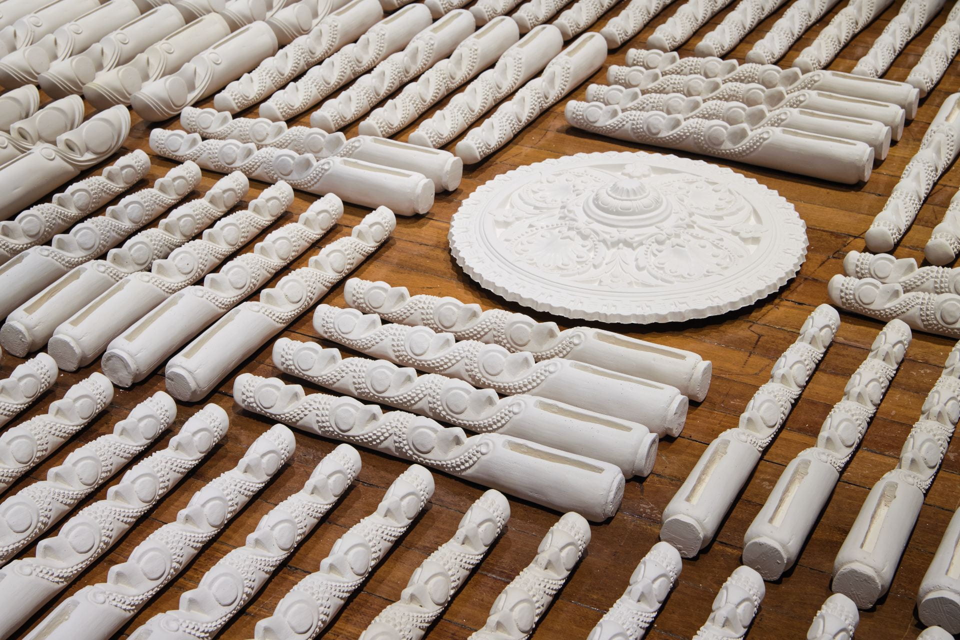 Rows of white carved sculptures placed on the floor surrounding a circular white plaster carving.